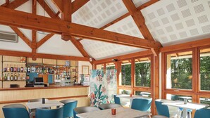 A bar area with wooden beams, a counter with various bottles, and seating with blue chairs and tables. - Hôtel Centre Port-Royal (Saint-Lambert)