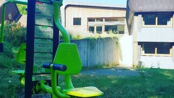 A green exercise machine in a grassy area with a building in the background.