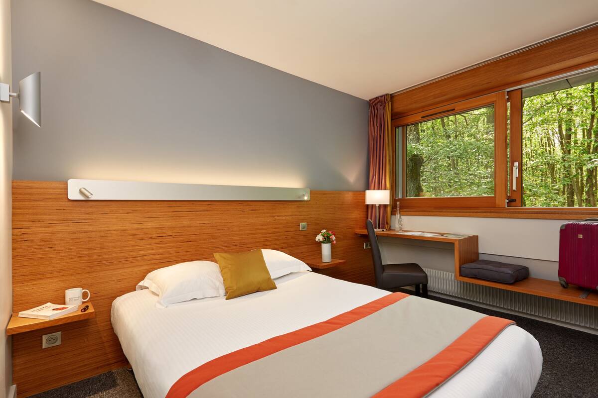 Une chambre d’hôtel avec un grand lit, un bureau, une chaise et une fenêtre donnant sur les arbres.