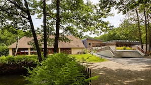 A two-story building with a sloped roof, surrounded by lush greenery and trees. - Hôtel Centre Port-Royal (Saint-Lambert)