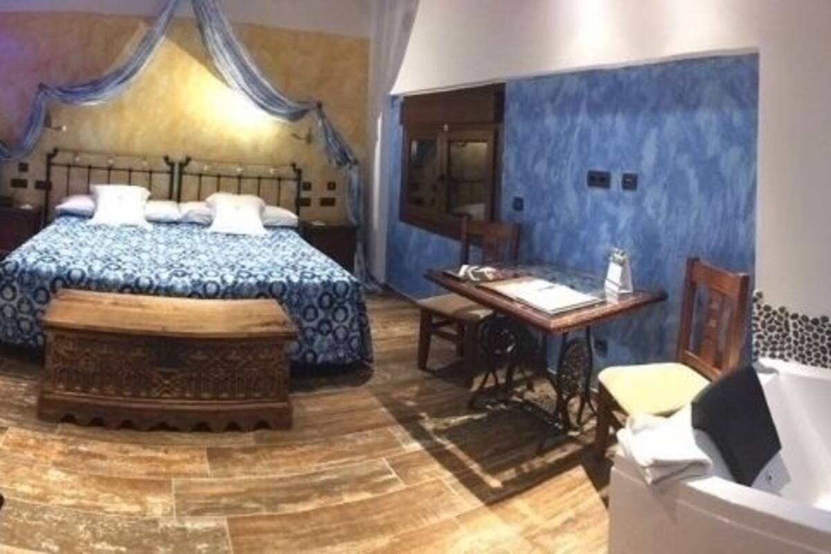 A bedroom with a large bed, a sitting area with a table and chairs, a bathtub, and a mirror.