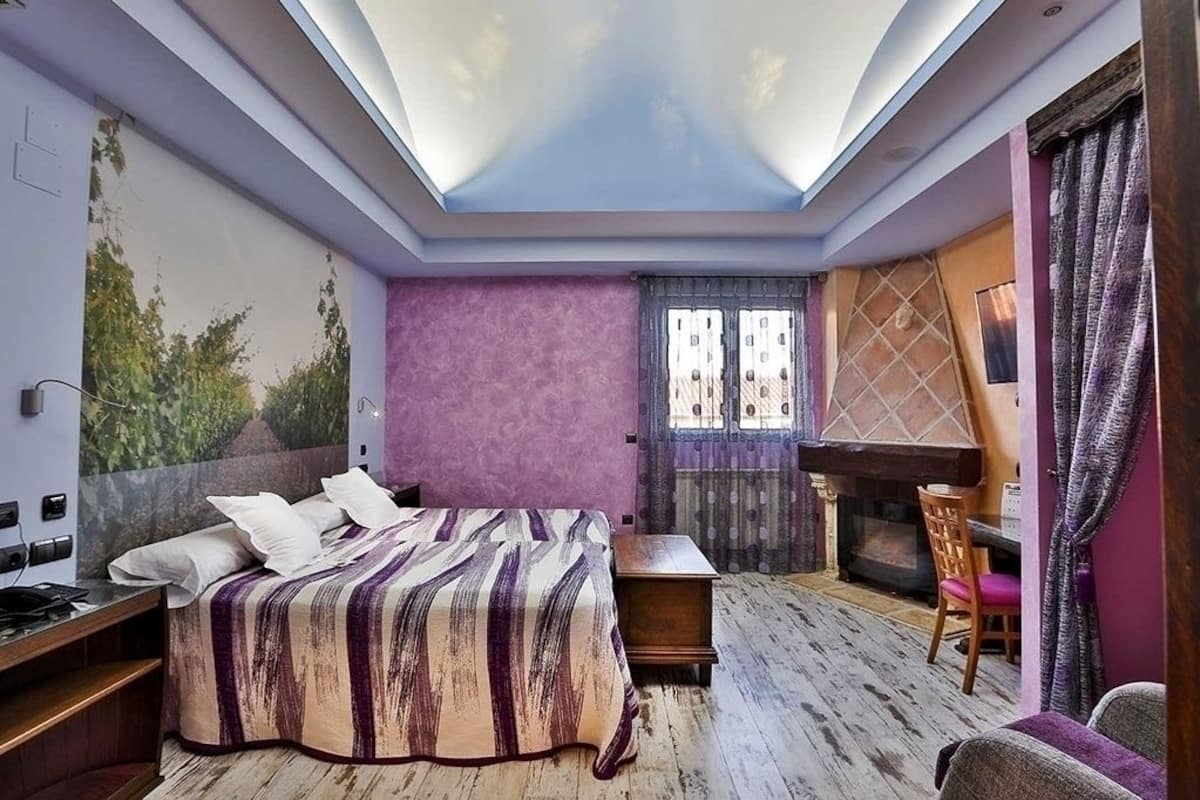 A bedroom with a bed, a desk, a chair, and a fireplace.