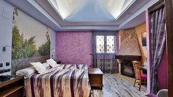 A bedroom with a bed, a desk, a chair, and a fireplace.