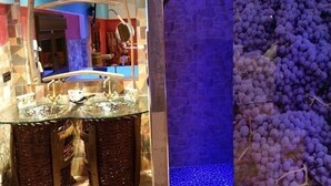 Un baño con lavamanos de vidrio, taburetes de mimbre y un espejo con un salpicadero de azulejos geométricos.