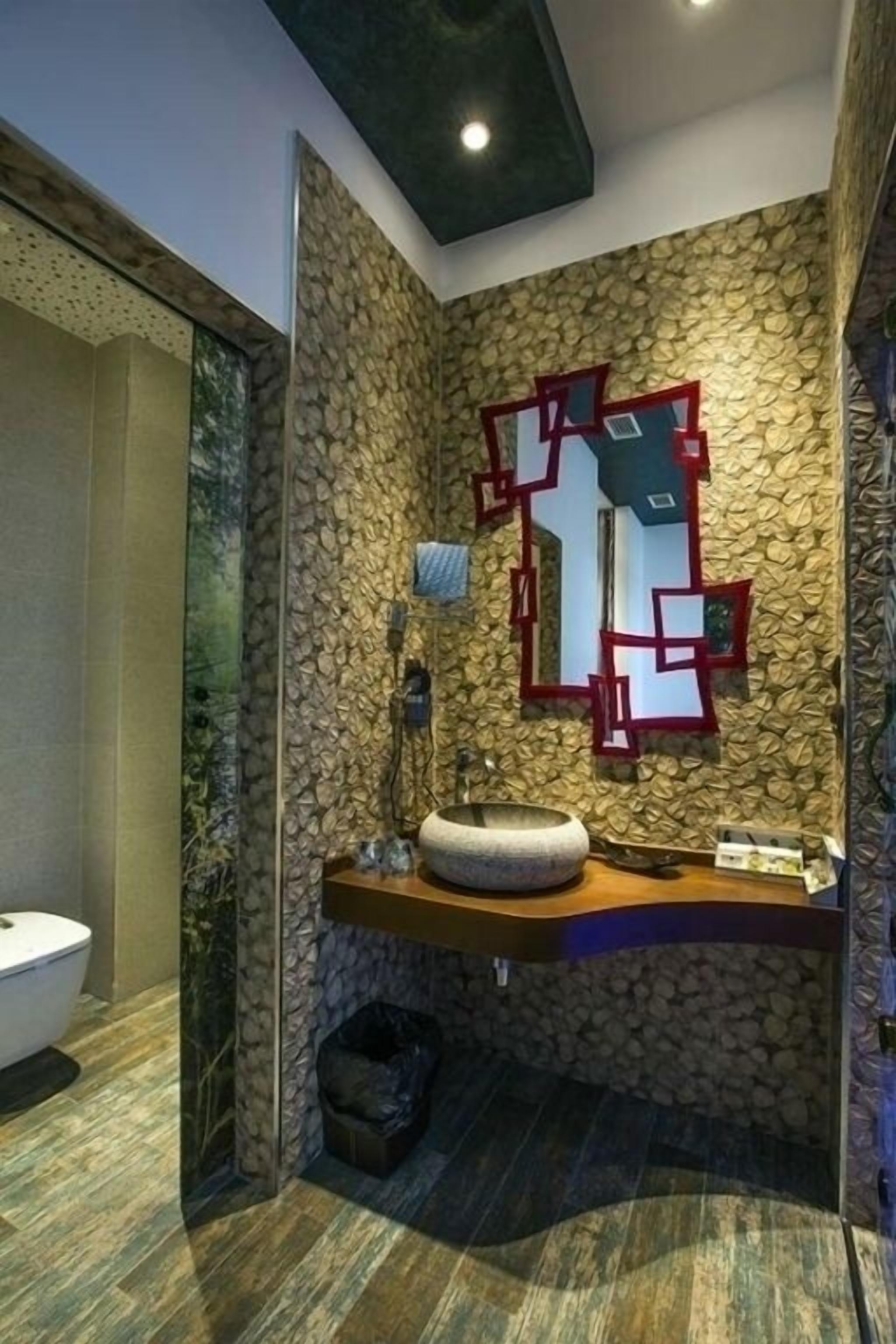 Un baño con pared de piedra, un lavabo con recipiente redondo y un espejo de marcos geométricos.
