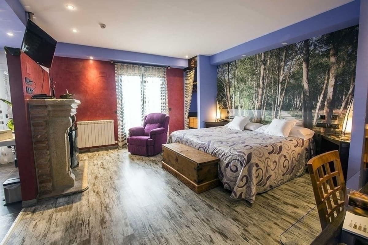 A bedroom with a bed, a chair, a wooden chest, a stone pillar, and a large forest mural on the wall.