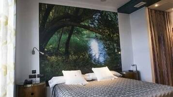 Un dormitori amb un òcul de bou circular, un llit amb un estovat estampat, una tauleta de nit i un mural gran amb motius de bosc.