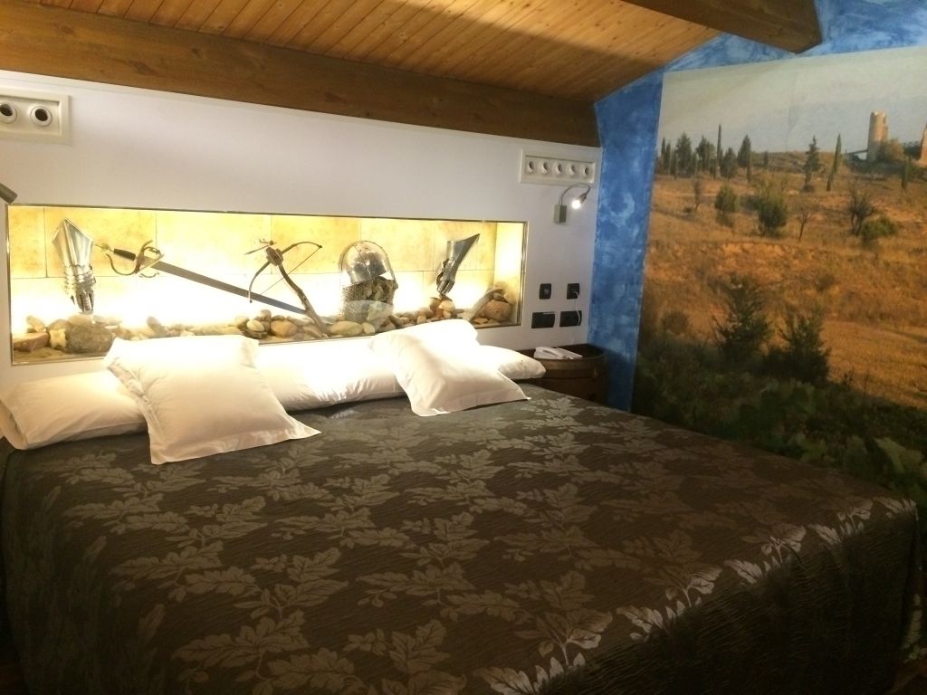 A bedroom with a bed, a headboard with lights, a nightstand, and a mural on the wall.
