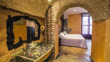 Una habitación con techo de piedra, lavamanos de cristal, cama con ropa de cama estampada y ventana con cortinas.
