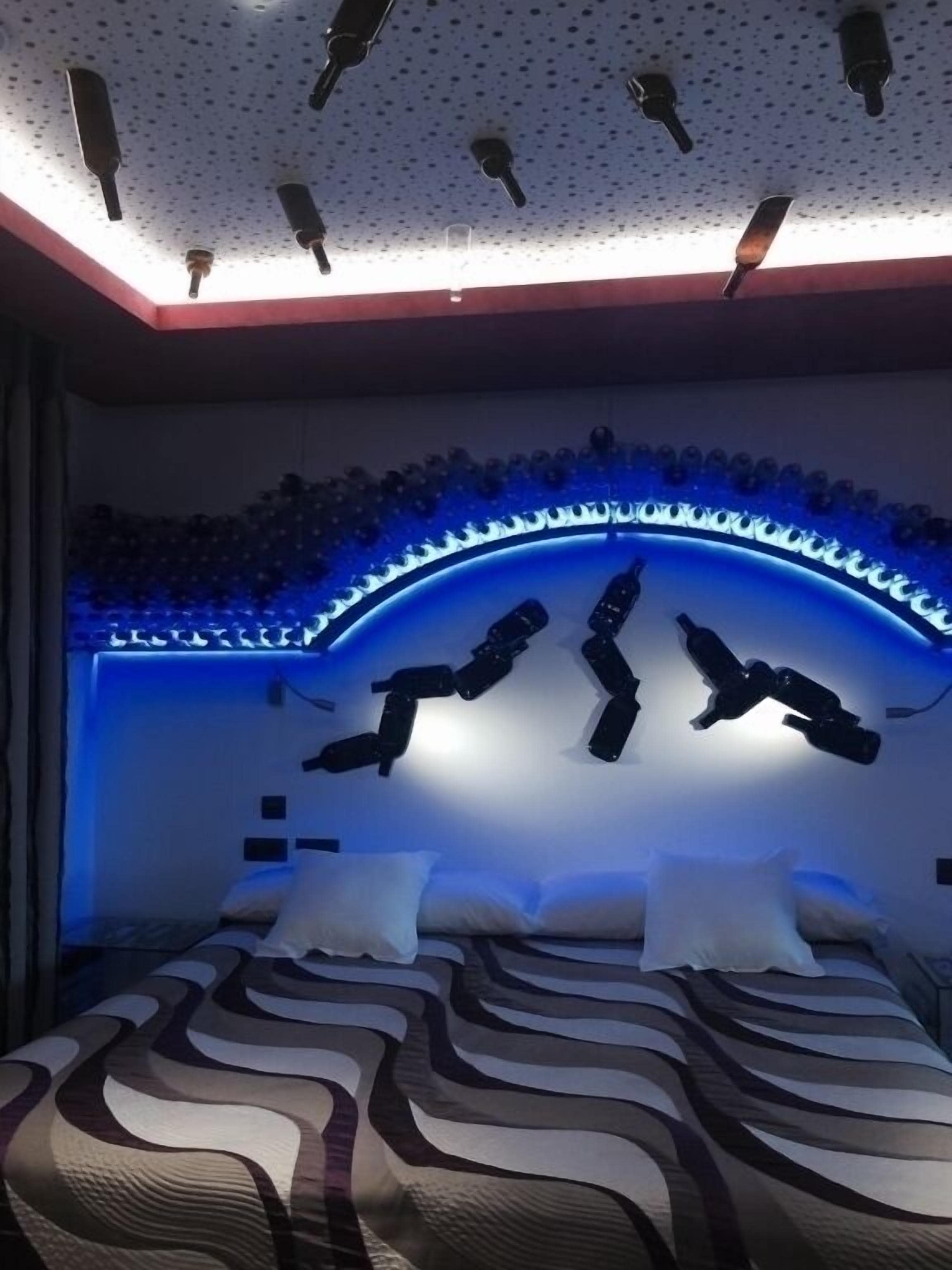 Un dormitorio con cama, techo con luces empotradas y una franja de luz azul en la pared.