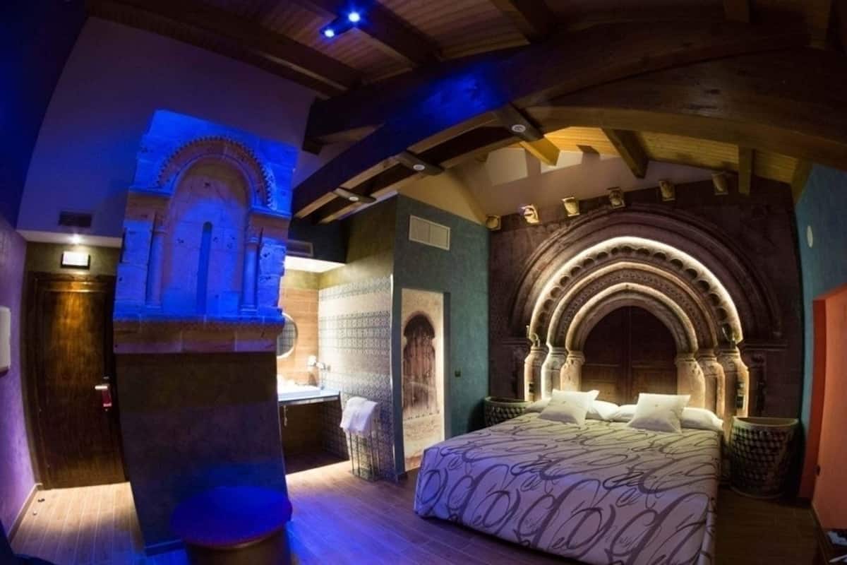A room with a bed, a small sitting area, and a large arched doorway.