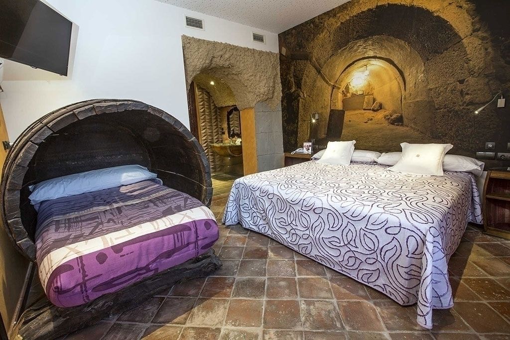 Une pièce dotée d’une arche en pierre, d’un lit avec une literie à motifs et d’un téléviseur fixé au mur.
