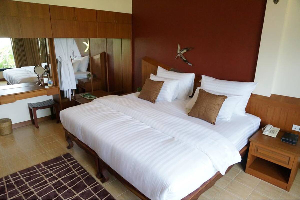 A hotel room with a large bed, a bedside table with a phone, a mirror, and a wooden headboard with a bird decoration.