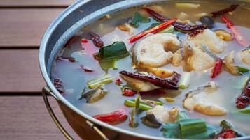 A pot of soup with visible ingredients like fish, green onions, and red chili peppers on a wooden table.