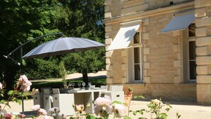 An outdoor seating area with a table and chairs, a large umbrella, and blooming roses. - Château Lagrave Béchade (Baleyssagues)