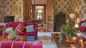A spacious living room with a red sofa, a coffee table, and a fireplace. There is a television and a chandelier in the room. - Château Lagrave Béchade (Baleyssagues)