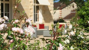 A stone building with a white awning and red cushions on a white sofa. - Château Lagrave Béchade (Baleyssagues)