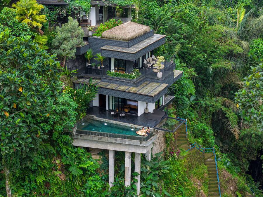 A multi-level modern house with a pool, surrounded by dense greenery.