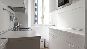 Una cocina moderna con un lavamanos de acero inoxidable, un microondas sobre la encimera y una ventana con persianas.