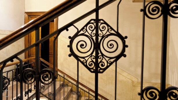 Una escalera con barandillas de metal negro ornamentadas y un pasamanos de madera.