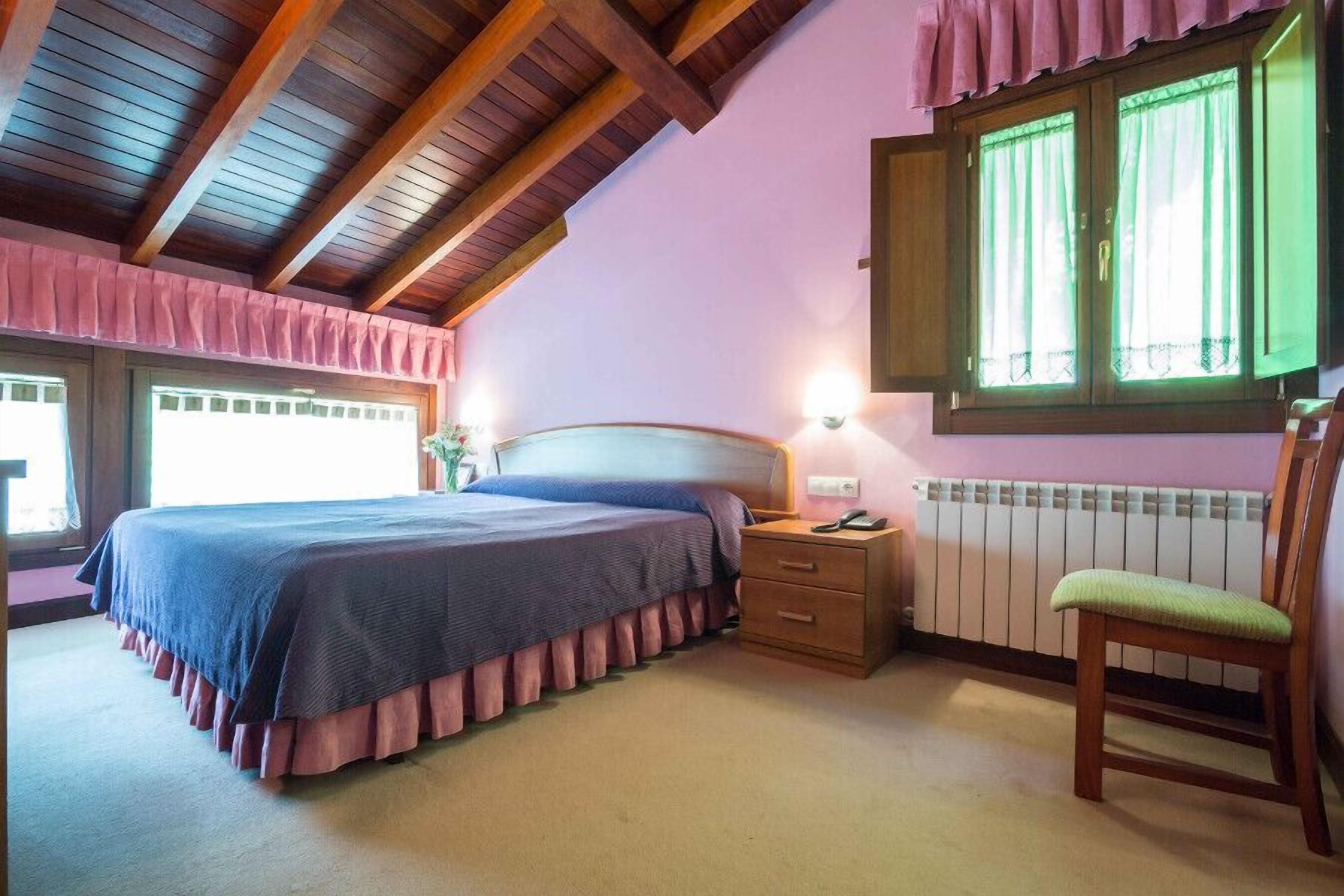 Ein Schlafzimmer mit Bett, Nachttisch, Stuhl und einem Fenster mit Vorhängen.