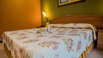 Un lit bien fait, recouvert d’une couvre-lit à motifs floraux, une table de chevet avec une lampe et un tableau accroché au mur.