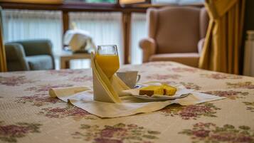 A dining table with a floral tablecloth, a glass of orange juice, a white cup, and a plate with a slice of cake.