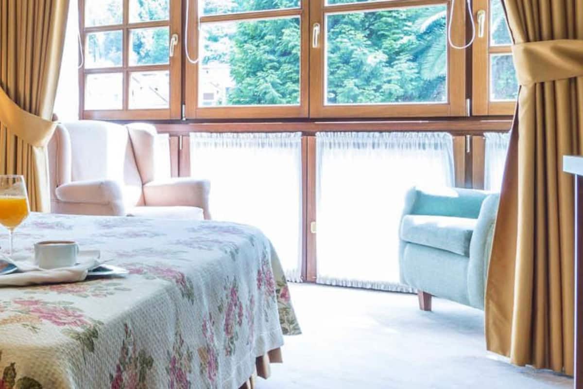 A hotel room with a bed, a bedside table with a phone, a tray with croissants, a glass of orange juice, and a chair by the window.