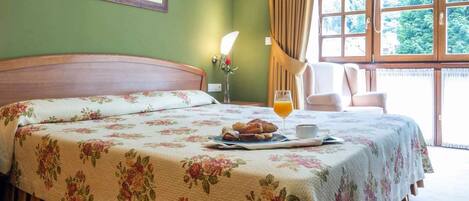 A hotel room with a bed, a bedside table with a phone, a tray with croissants, a glass of orange juice, and a chair by the window.