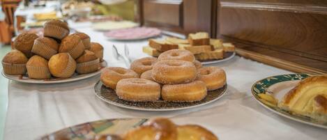 A buffet table with various baked goods including muffins, donuts, and pastries.