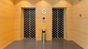 L’intérieur d’un ascenseur avec des murs en bois, deux portes marquées de la lettre « G », une poubelle et un détecteur d’incendie.