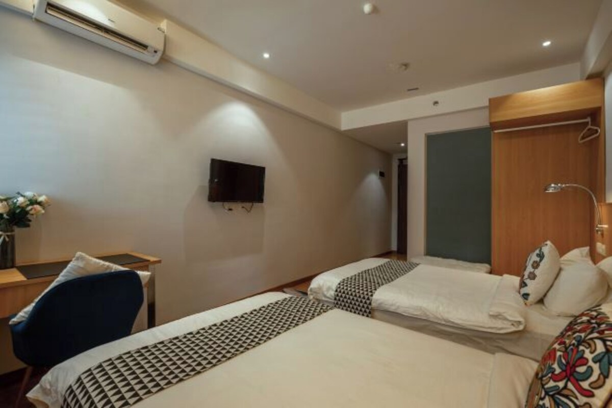 A hotel room with two beds, a desk, a chair, a TV, and an air conditioning unit.
