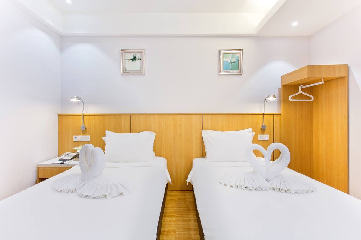 Ein Hotelzimmer mit zwei Betten, einem hölzernen Kopfteil, weißen Bettwäsche, zwei Wandlampen und einem Holzschrank.