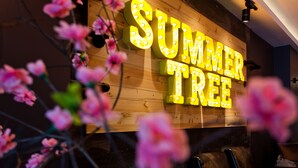 Un mur en bois avec une enseigne lumineuse indiquant « SUMMER TREE » et des fleurs roses au premier plan.