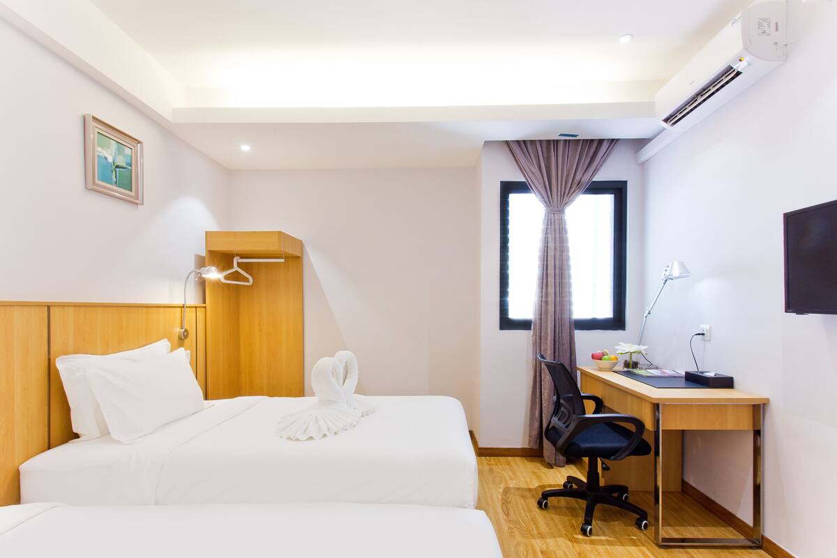 Ein Hotelzimmer mit zwei Betten, einem Schreibtisch, einem Sessel, einem Fernseher und einer Klimaanlage.