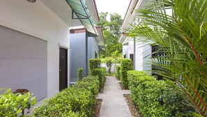 A narrow pathway flanked by neatly trimmed hedges and a palm tree, leading to a building with a grey facade and a dark door. - Modern Resort at Naiyang (Sa Khu)