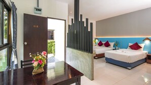 A modern hotel room with a large bed, a separate sofa bed, a dining table with a vase of flowers, and a view of greenery outside. - Modern Resort at Naiyang (Sa Khu)