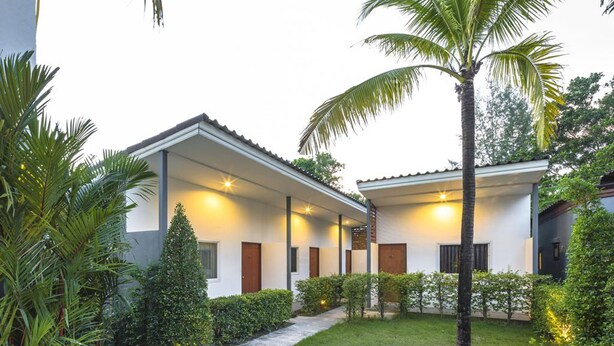 A modern building with a covered walkway, palm trees, and a well-maintained lawn. - Modern Resort at Naiyang (Sa Khu)
