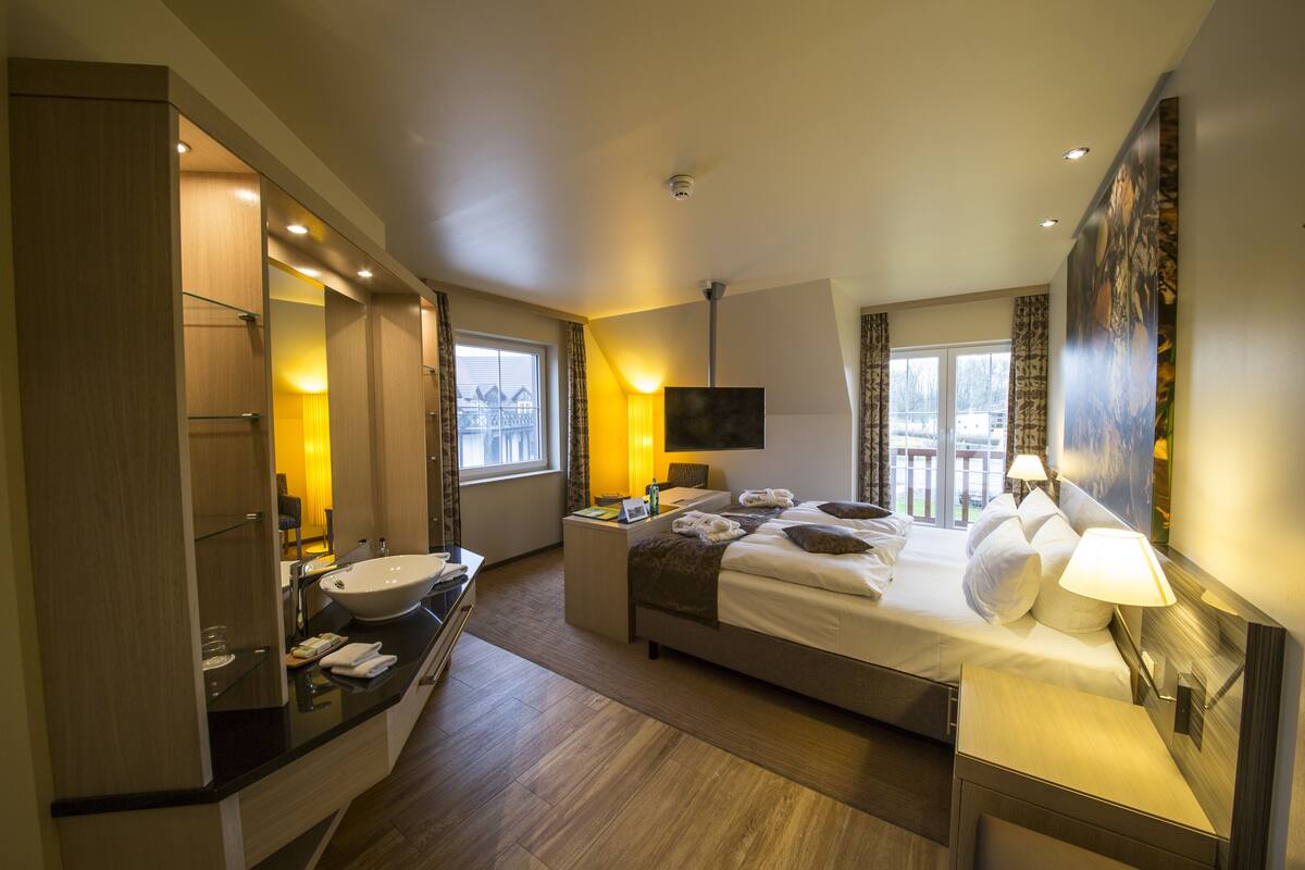 A hotel room with a bed, bedside table, lamp, and a large window.