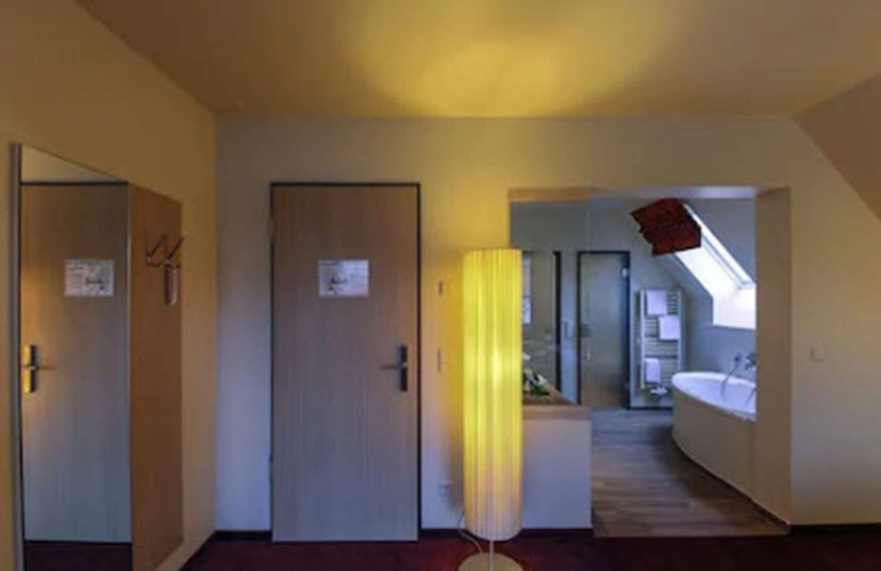 A hotel room with a door, a lamp, and a view into a bathroom with a bathtub.