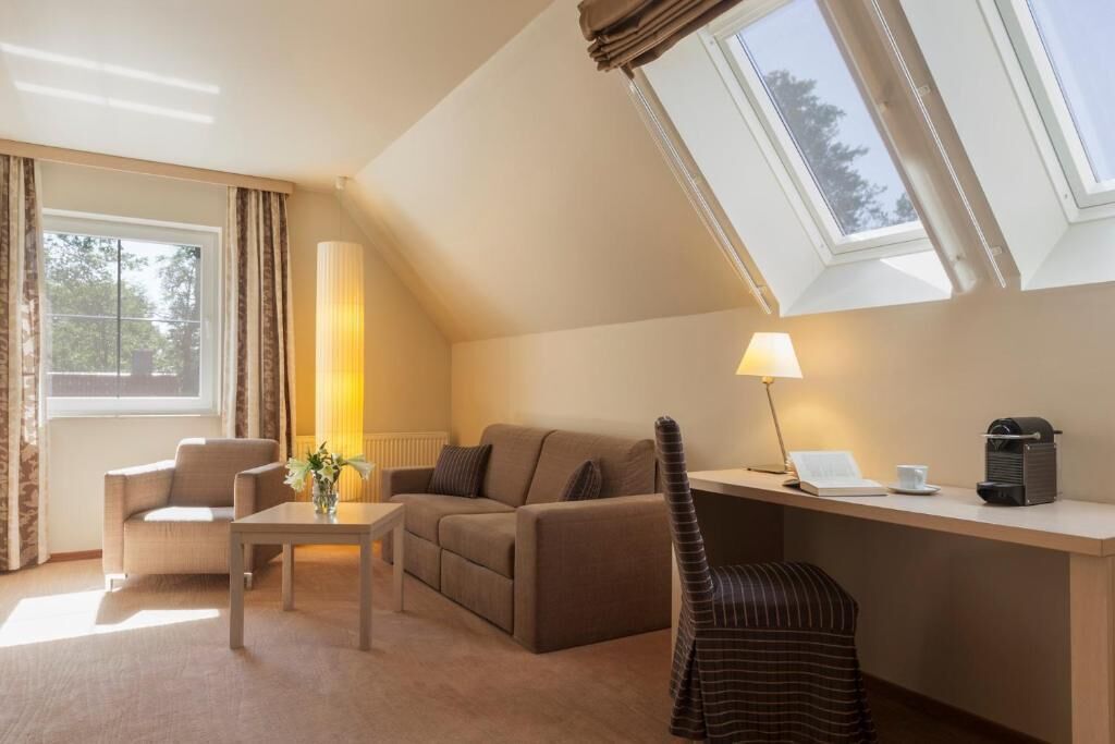 Una habitación acogedora con un sofá, una silla, una mesa, una lámpara y una cafetera.