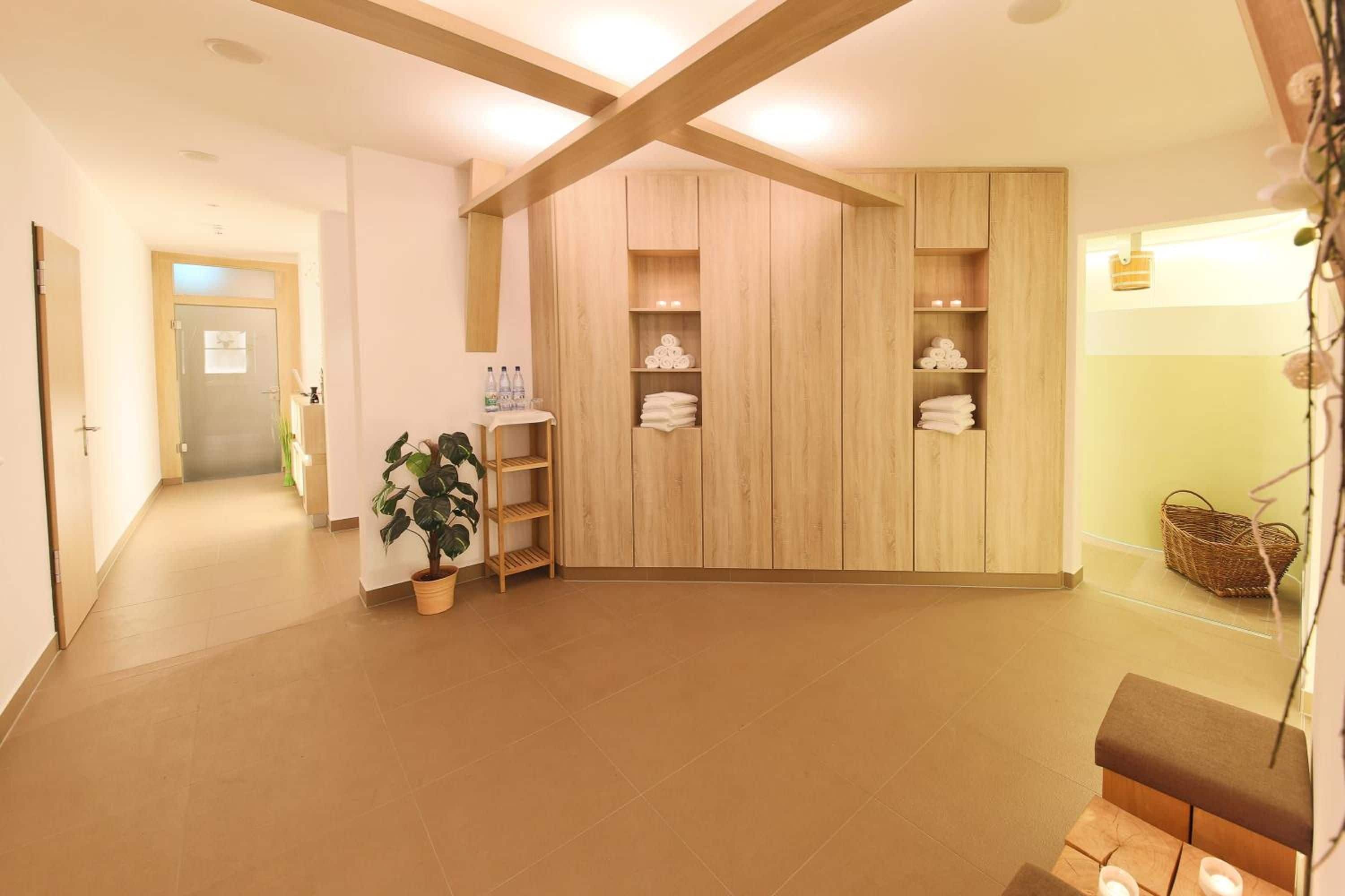 Habitación de hotel con un armario de madera, una mesita con artículos de aseo, una planta en maceta y un banco.