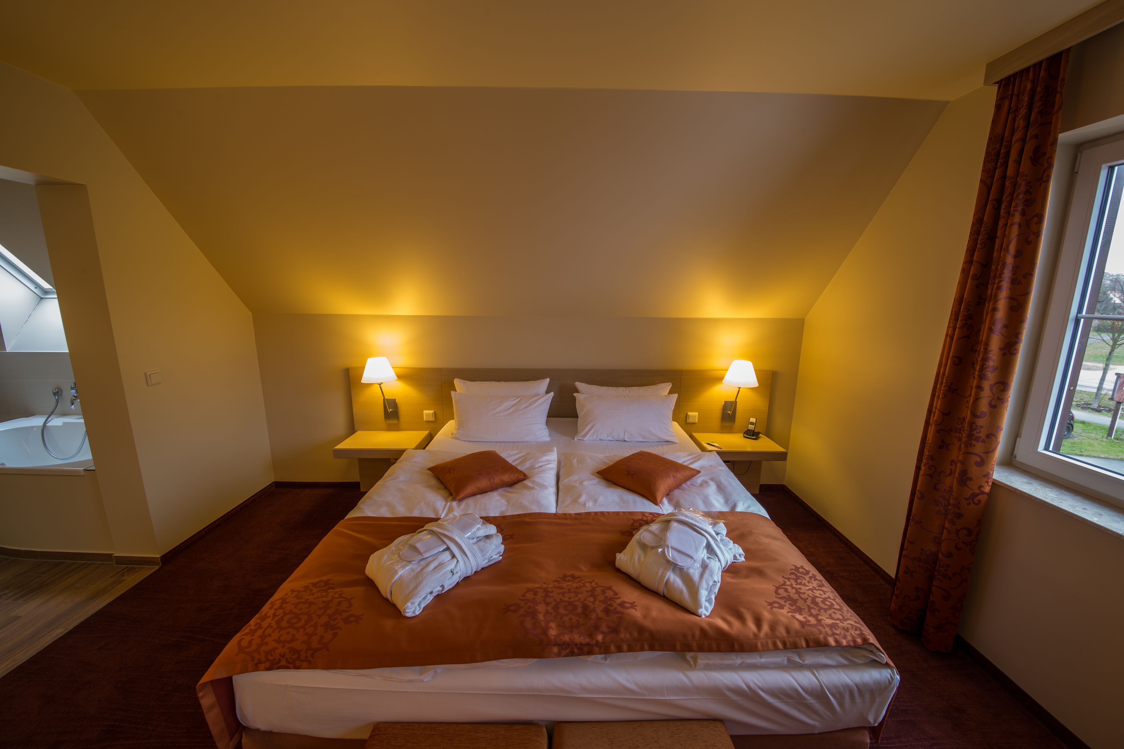 Habitación de hotel con una cama grande, dos mesitas de noche con lámparas, una ventana con cortinas y vistas al exterior.