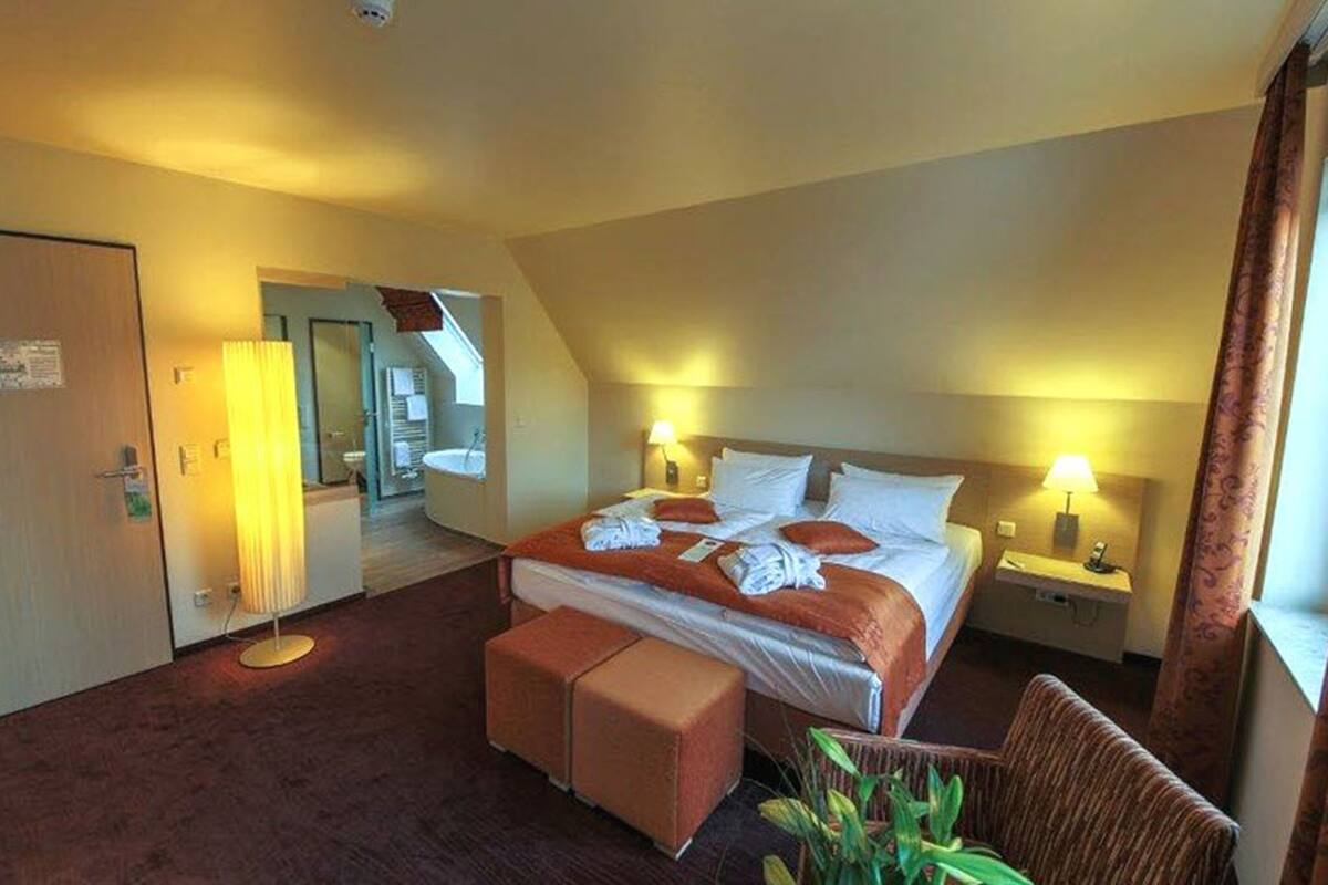 A hotel room with a large bed, two bedside tables with lamps, a small seating area, and a door leading to another room.
