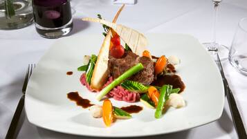 Un plato cuadrado blanco con un bistec, verduras y salsa.