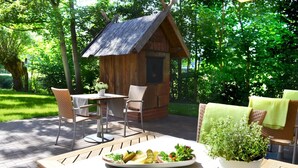 An outdoor dining area with a wooden table, wicker chairs, and a small wooden structure in the background.