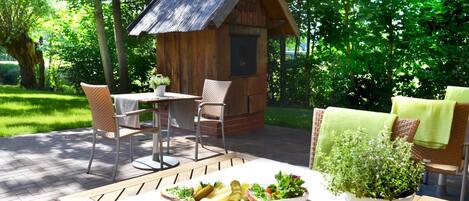An outdoor dining area with a wooden table, wicker chairs, and a small wooden structure in the background.