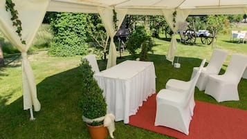 Ein mit Zelten überspanntes Außenbereich mit Tisch und Stühlen, einem roten Teppich und viel Grün.