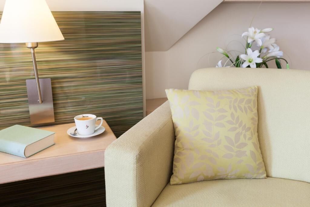 Une chambre d’hôtel avec un canapé, une table de chevet avec une lampe, une tasse de café et un arrangement floral.