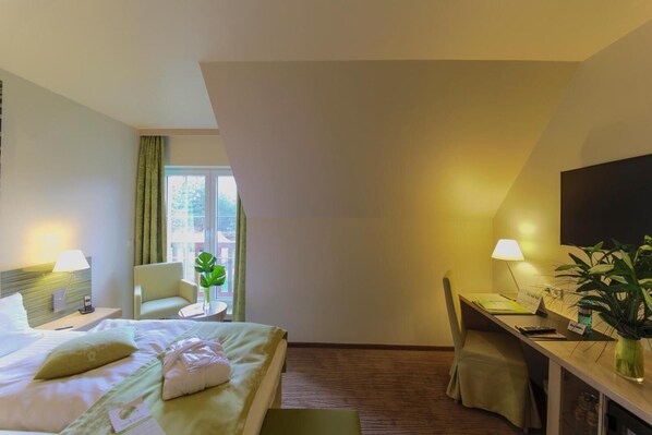 Habitación de hotel con cama, escritorio, silla, televisor y ventana con cortinas.